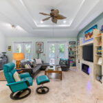 A spacious living room with turquoise and leather seating, a large TV, and a view of the backyard through glass doors, offering a comfortable and inviting space for guests.