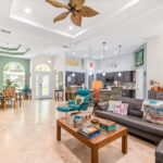 Open-concept living room with a large sectional sofa, colorful decor, and a view into the dining area and kitchen, all bathed in natural light from large windows.