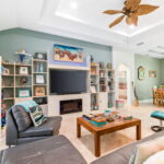 Spacious living room with cozy seating, a large flat-screen TV, and a vibrant, beach-themed decor, opening to a dining area with colorful furnishings.