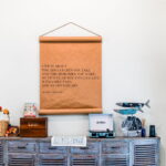 A wall featuring a large inspirational quote on a scroll, set above a rustic wooden cabinet adorned with a vintage-style record player and charming decorative items.