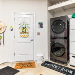 A laundry room featuring a modern stacked washer and dryer, with a pineapple 