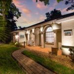 Illuminated exterior of St. Augustine Guest House at dusk, featuring arched windows, a cozy seating area, and a well-maintained garden path.