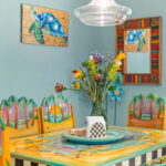 Dining area featuring hand-painted chairs and table with tropical designs, colorful wall art, and a decorative flower centerpiece in a vacation rental.