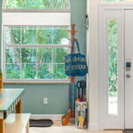 Entrance area of St. Augustine Guest House featuring a bright window with tropical garden views, colorful decor, and a bag with the phrase 