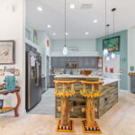 A bright and open kitchen with colorful wooden bar stools, modern gray cabinets, and elegant lighting, offering a welcoming space for cooking and socializing.