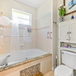 Coastal-themed bathroom with a tub and etched glass featuring a lighthouse design, white cabinet with amenities, and nautical decor in a vacation rental.